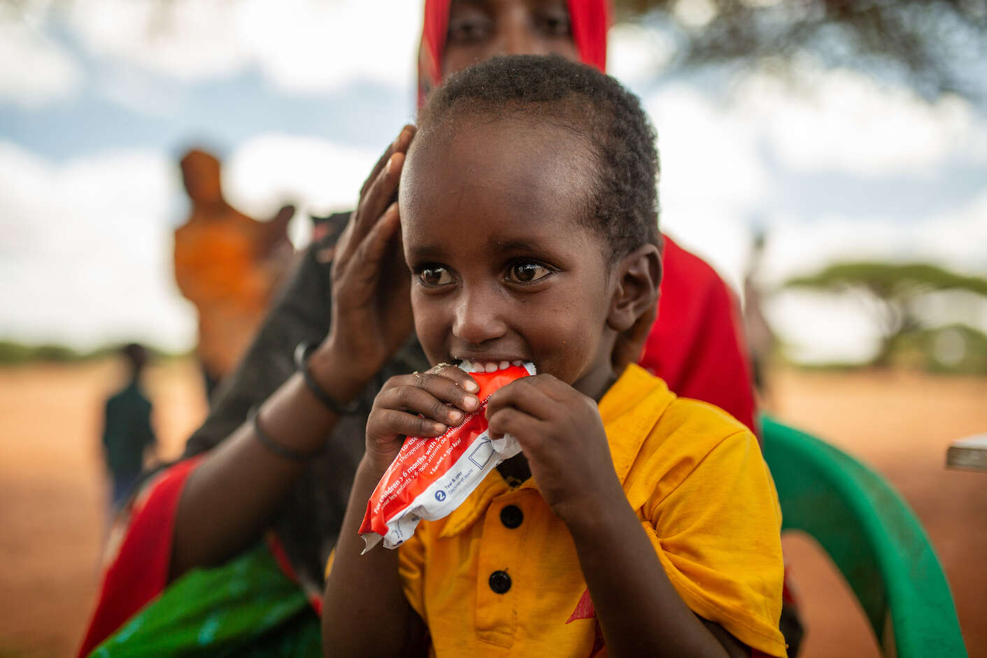 한 어린이가 엄마의 품에서 영양식을 먹고 있습니다. 