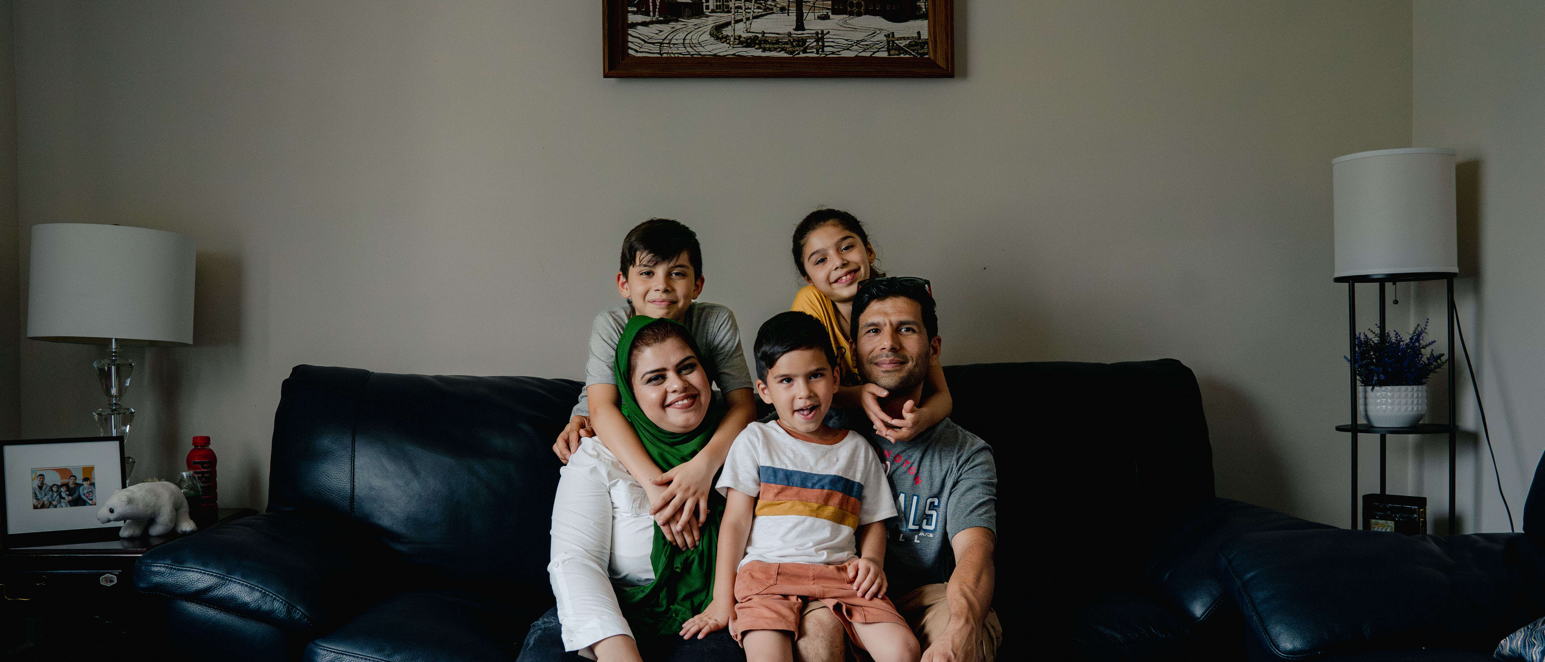A family sits together on a couch and poses for a photo.