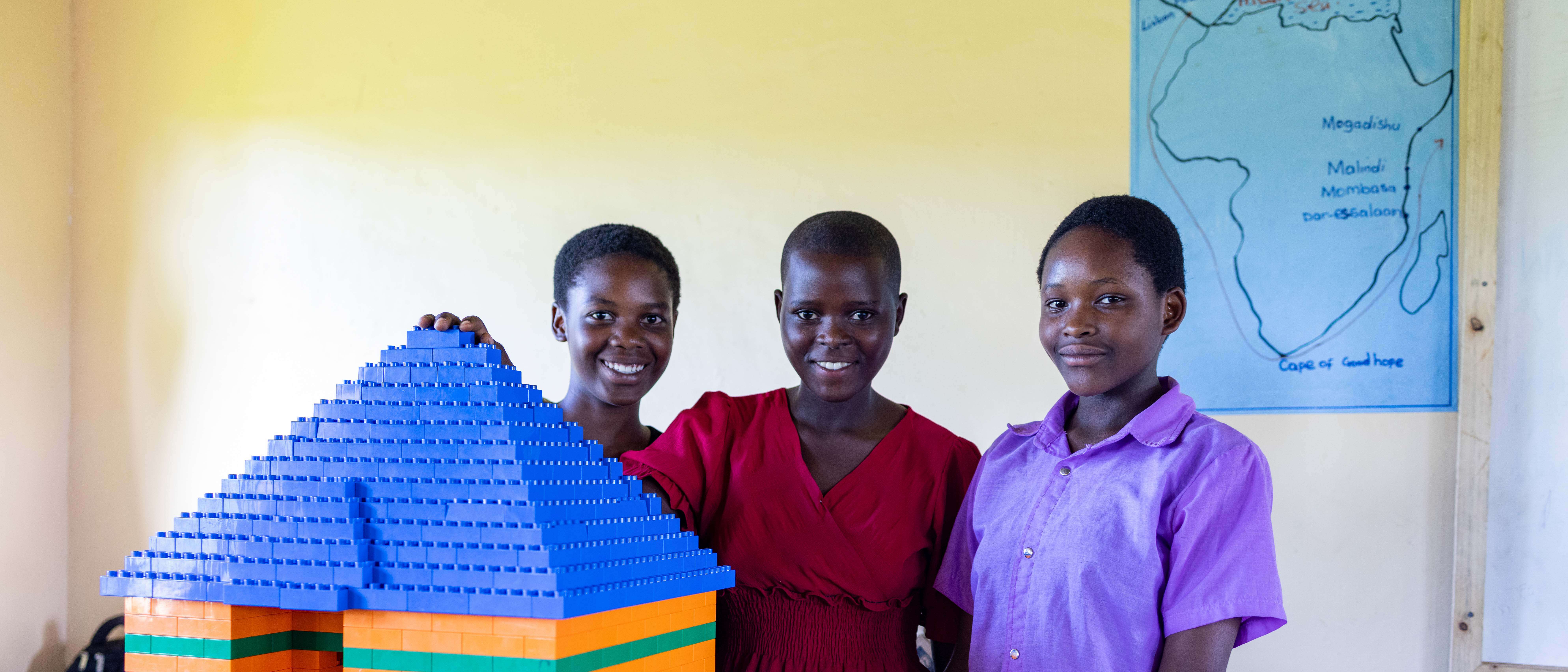 Three students smile and pose for a photo in a school in Uganda.